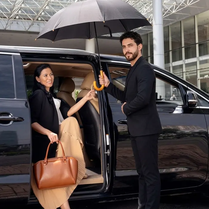 Driver holding an umbrella and opening the door for a traveller